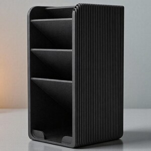 May include: A black desk organizer with three angled compartments and a ribbed exterior. The organizer is made of a solid material and has a minimalist design. It is suitable for storing pens, pencils, and other office supplies.