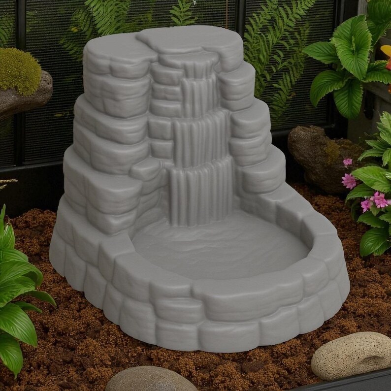Puede incluir: Una fuente de cascada gris escalonada con una cuenca. La fuente tiene un dise&ntilde;o rocoso y en capas, con agua cayendo en cascada por m&uacute;ltiples niveles. La fuente est&aacute; rodeada de tierra marr&oacute;n y vegetaci&oacute;n.