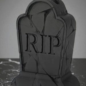 May include: A black tombstone with the letters "RIP" carved into the front. The tombstone has a textured surface and a rounded top. The base is rectangular. This item is likely a Halloween decoration.