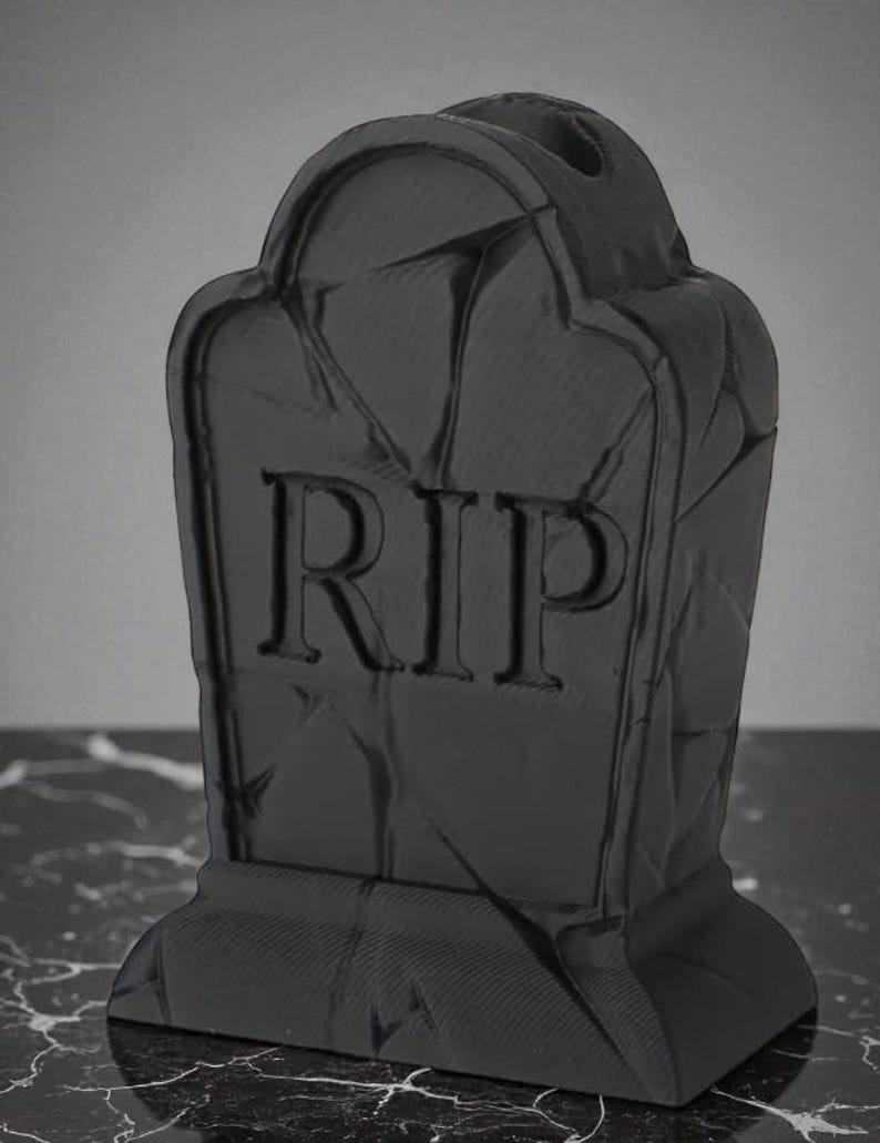 May include: A black tombstone with the letters "RIP" carved into the front. The tombstone has a textured surface and a rounded top. The base is rectangular. This item is likely a Halloween decoration.