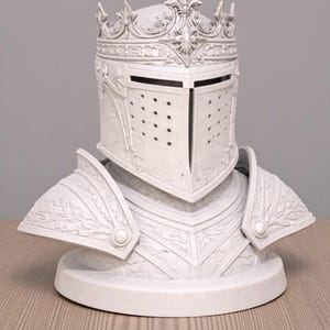 May include: A white decorative bust of a knight's helmet and armor. The helmet features a crown and a visor with small holes. The armor includes shoulder guards and chest plates, all with detailed relief patterns.