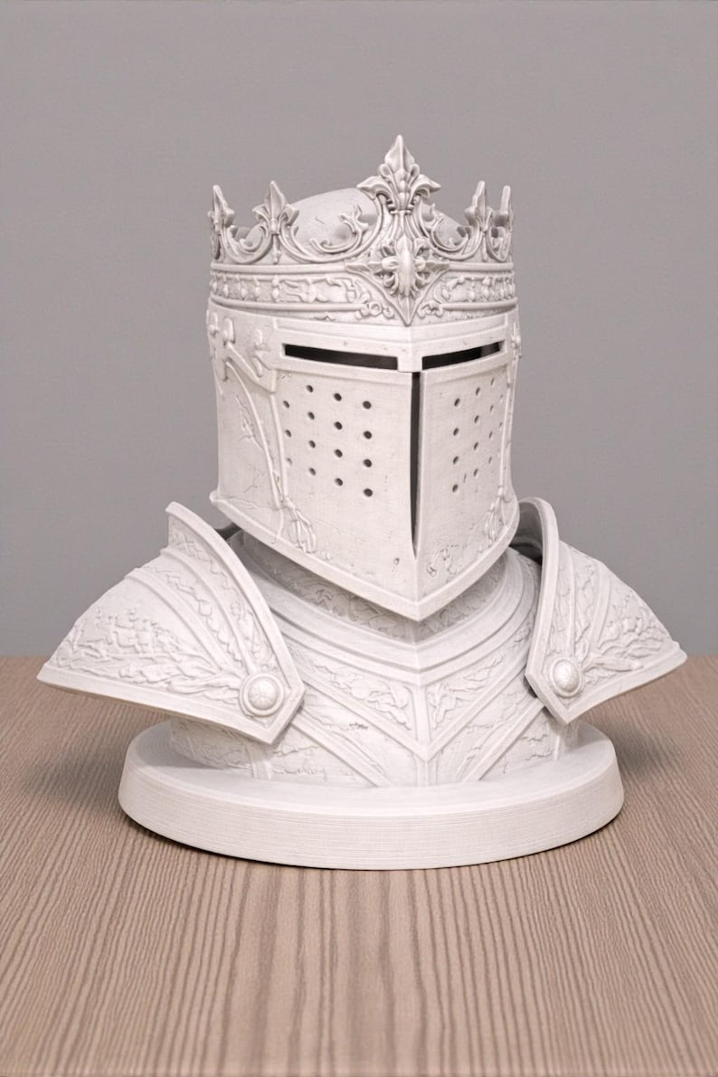 May include: A white decorative bust of a knight's helmet and armor. The helmet features a crown and a visor with small holes. The armor includes shoulder guards and chest plates, all with detailed relief patterns.