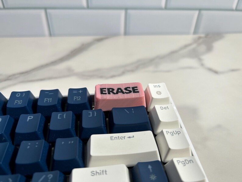 May include: A close-up of a keyboard with a pink keycap that says "ERASE" in black lettering. The keyboard has blue and white keys.