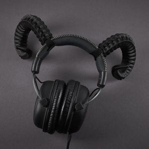 May include: Black over-ear headphones with a distinctive design. The headphones feature curved, horn-like attachments on the headband. The earcups are round and padded. The headphones are wired and set against a dark grey background.