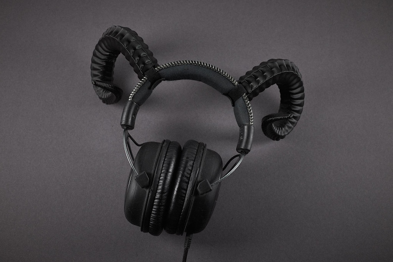 May include: Black over-ear headphones with a distinctive design. The headphones feature curved, horn-like attachments on the headband. The earcups are round and padded. The headphones are wired and set against a dark grey background.