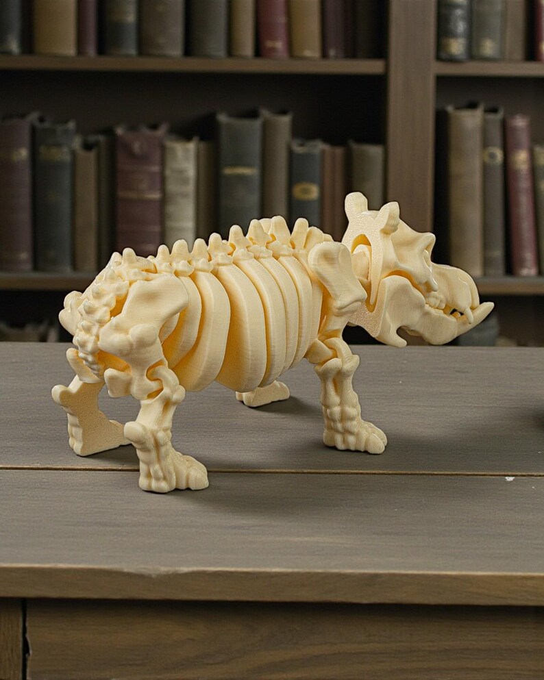 May include: A cream-colored, 3D-printed model of a prehistoric animal skeleton, possibly a dinosaur or similar creature. The model is detailed, showing ribs, spine, and skull. It stands on a wooden surface, with a blurred bookshelf background.