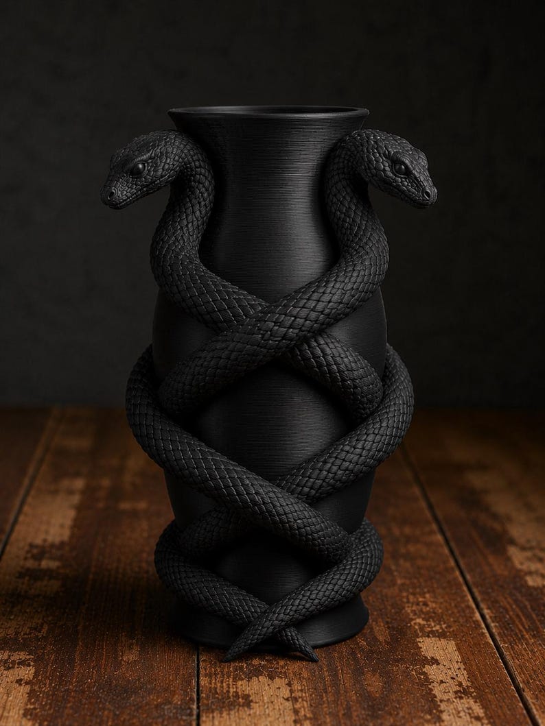 May include: A matte black vase with two snakes coiled around it. The snakes' bodies intertwine, and their heads face outward. The vase has a textured surface and sits on a wooden surface. The snakes have detailed scales.