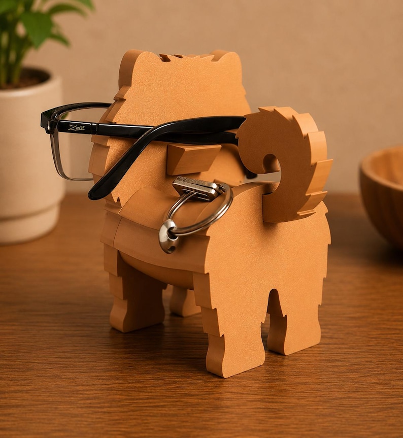 May include: A light brown, dog-shaped eyeglasses and key holder. The holder has a slot for glasses and a ring for keys. Black eyeglasses are resting on the holder. The holder is made of wood and has a textured appearance.