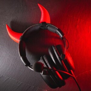 May include: Black headphones with a red devil horn headband. The headphones have a microphone attached.