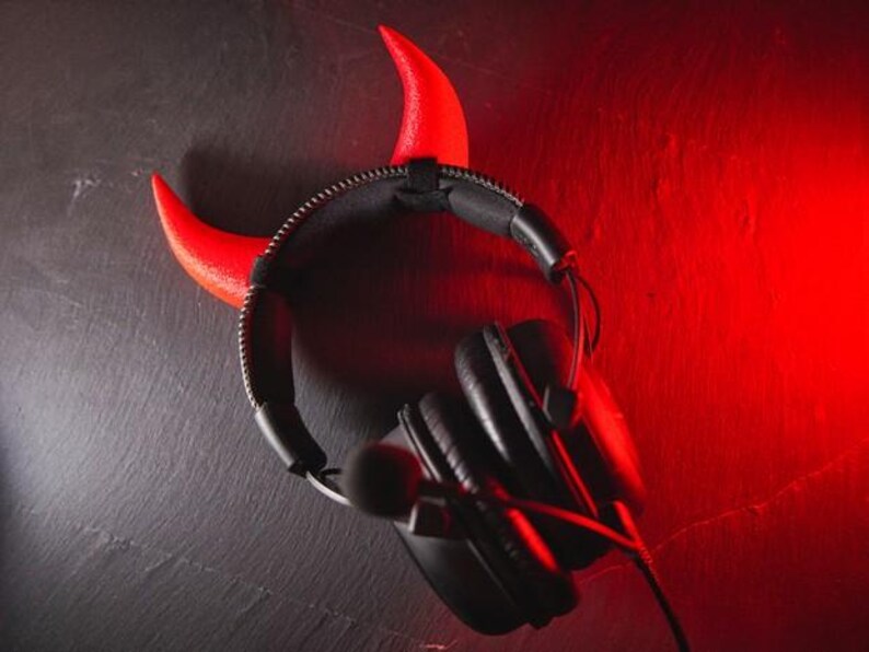 May include: Black headphones with a red devil horn headband. The headphones have a microphone attached.