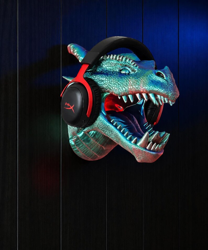 May include: A wall-mounted dragon head sculpture in shades of blue and green, with red accents inside the mouth. Black and red gaming headphones are placed on the dragon's head. The dragon's mouth is open, revealing sharp teeth.