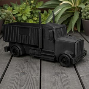 K&ouml;nnte beinhalten: Ein schwarzer dekorativer LKW-Pflanzk&uuml;bel mit rechteckiger Ladefl&auml;che, zwei Auspuffrohren und einem detaillierten Frontgrill. Der LKW besteht aus einem festen Material und steht auf einer grauen Holzoberfl&auml;che, mit gr&uuml;nen Pflanzen im Hintergrund.
