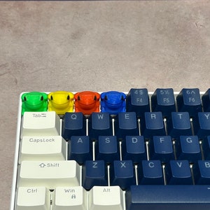 May include: A keyboard with blue keys and white keycaps. Four frog-shaped keycaps are placed on the top row of the keyboard. The frog keycaps are green, yellow, orange, and blue.