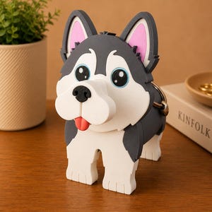 May include: A whimsical, cartoon-style Husky dog figurine. The dog has a gray and white coat, large blue eyes, and a red tongue. The figurine is standing on a wooden surface. A small plant in a beige pot is in the background.