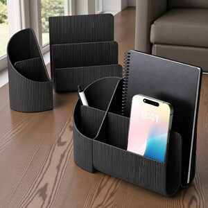 May include: A set of black desk organizers, including a pen holder, a multi-compartment organizer, and a file holder. A smartphone with a colorful screen and a notebook are also visible. The organizers have a ribbed texture.
