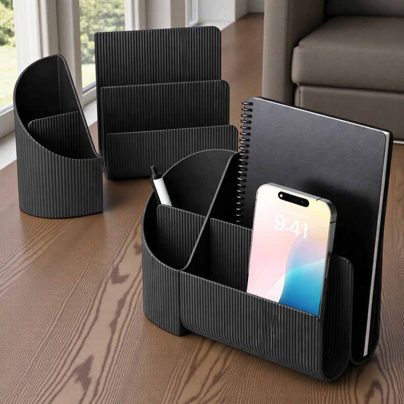 May include: A set of black desk organizers, including a pen holder, a multi-compartment organizer, and a file holder. A smartphone with a colorful screen and a notebook are also visible. The organizers have a ribbed texture.
