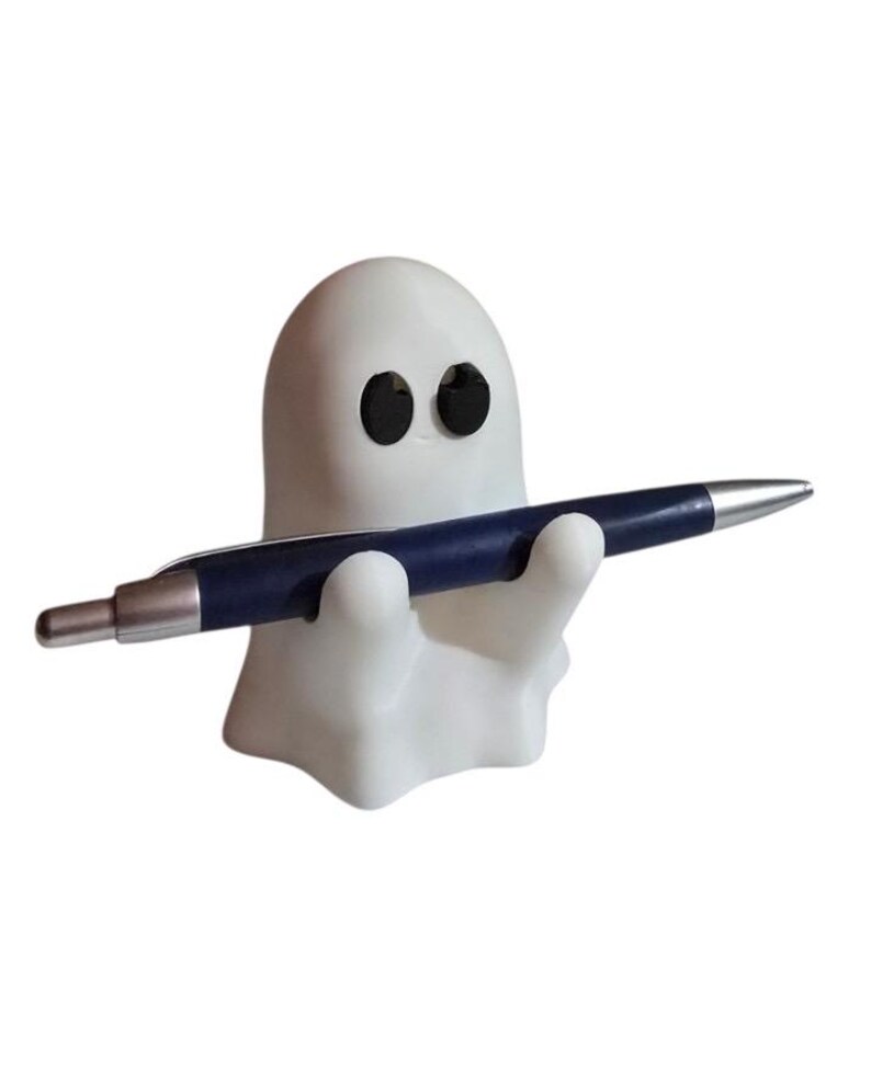 May include: A white ghost-shaped pen holder with black eyes, holding a blue and silver pen. The pen holder is a whimsical desk accessory, perfect for adding a touch of fun to any workspace. The pen is approximately 5.5 inches long.