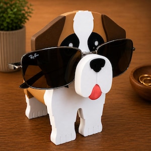 May include: A wooden dog-shaped sunglasses holder in white, brown, and black, with a red tongue. The holder is wearing a pair of black sunglasses with silver frames. The Ray-Ban logo is visible on the left lens.