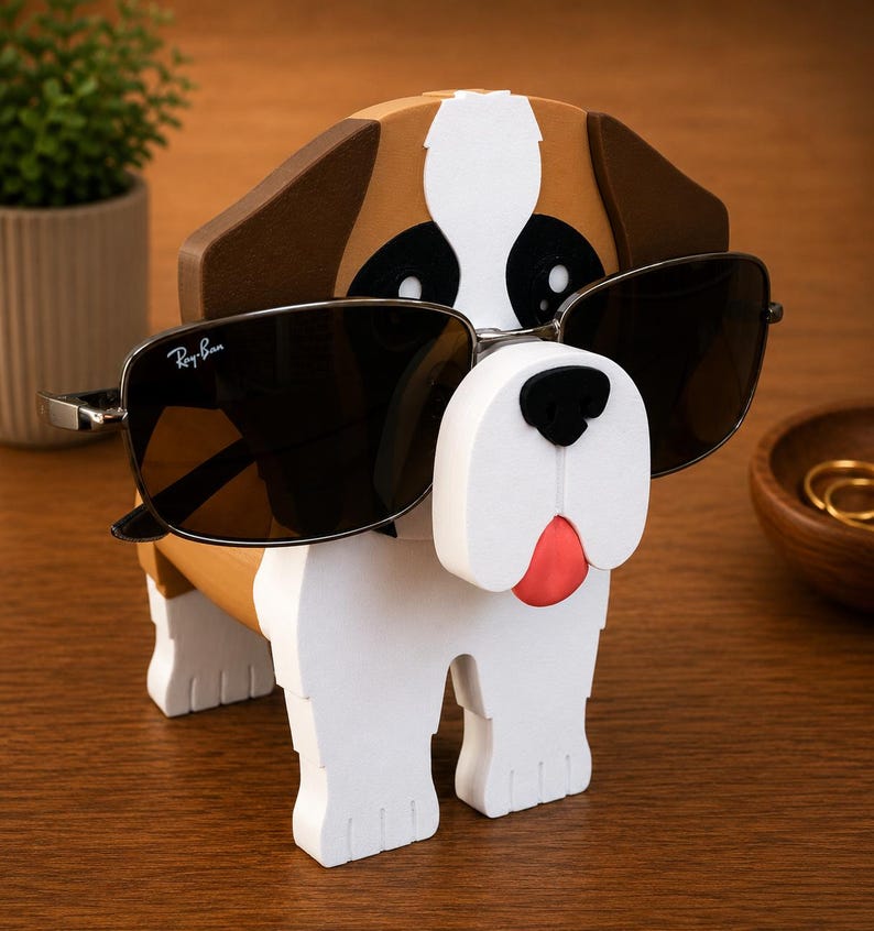 May include: A wooden dog-shaped sunglasses holder in white, brown, and black, with a red tongue. The holder is wearing a pair of black sunglasses with silver frames. The Ray-Ban logo is visible on the left lens.