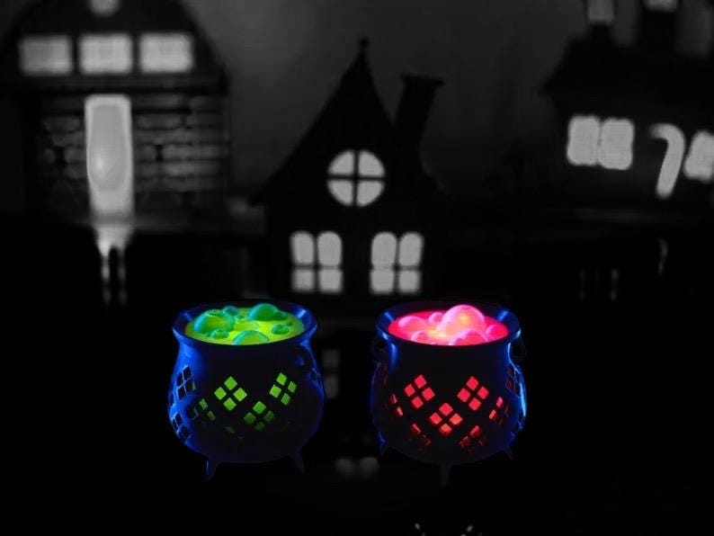 May include: Two black cauldrons with glowing green and red liquid inside. The cauldrons have a decorative design and are lit from within.