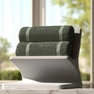 May include: Two rolled green towels with a light stripe detail are stacked on a white, modern-style holder. The towels are made of a soft, absorbent material. The holder is made of a smooth, solid material.