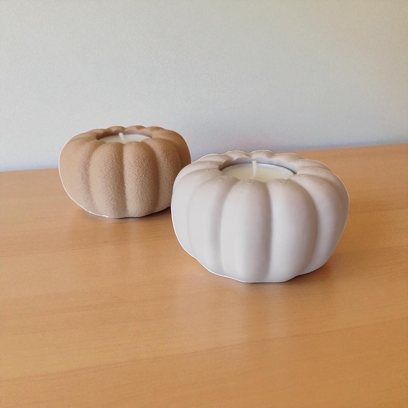 Puede incluir: Dos velas con forma de calabaza en colores neutros sobre una superficie de madera. Una es beige claro, la otra blanca suave. Cada vela tiene un centro de cera blanca, creando una est&eacute;tica oto&ntilde;al y acogedora. Las velas son decorativas y adecuadas para la decoraci&oacute;n del hogar.
