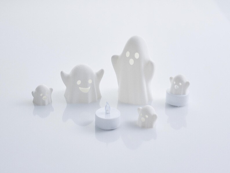 May include: Set of five white ceramic ghost candle holders with different facial expressions. The ghosts are various sizes and are lit with tea lights.