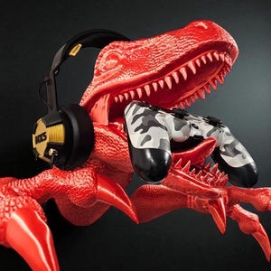 May include: A red dinosaur sculpture holding a camouflage-patterned game controller. A black and yellow headset rests on the dinosaur's head. The headset has the text "HXS" on the side.