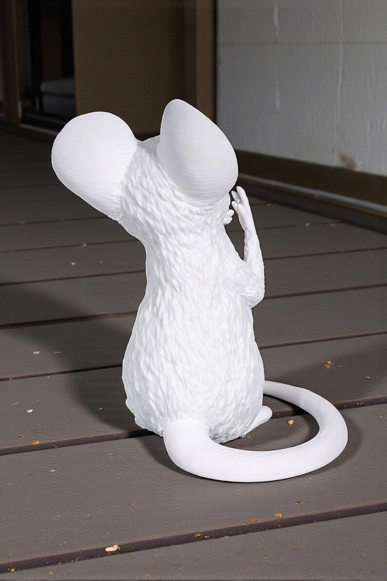 May include: A white sculpture of a mouse with oversized ears and a long, curved tail. The mouse is depicted from the back, with its hand raised near its head. The sculpture has a textured surface and is set against a neutral background.