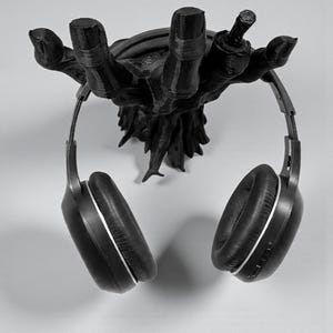 K&ouml;nnte beinhalten: Schwarzer, 3D-gedruckter Kopfh&ouml;rerhalter in Form einer Hand. Der Halter ist an einer Wand montiert und tr&auml;gt ein Paar schwarze Kopfh&ouml;rer mit silbernen Akzenten. Das Design ist eine einzigartige und k&uuml;nstlerische Art, Kopfh&ouml;rer aufzubewahren.