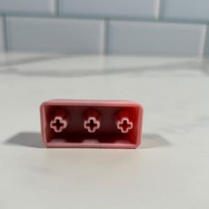 May include: A pink plastic keycap with three cross-shaped keycaps.
