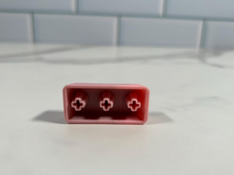 May include: A pink plastic keycap with three cross-shaped keycaps.