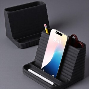 May include: Two dark gray desk organizers with a ribbed design. One organizer holds a smartphone displaying the time 9:41, a pencil, and scissors. The other organizer is empty. A white pen rests in the front tray of the organizer with the phone.