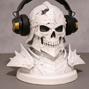 May include: A white skull bust wearing a black and gold pair of headphones. The skull is detailed with cracks and a helmet, and is wearing a detailed chest piece. The headphones are over-ear style.