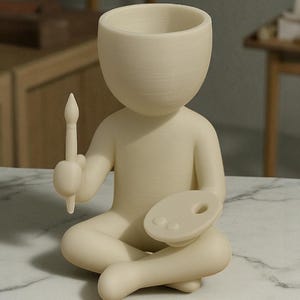 May include: A cream-colored figurine of a person seated cross-legged, holding a paintbrush and a palette. The figure has a large, open head, suggesting a vase or planter. The overall design is minimalist and artistic.