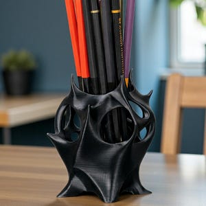 May include: A black, 3D-printed pencil holder with a unique, spiky design. The holder contains several pencils in various colors, including red, black, and purple. The pencils are of standard size, approximately 7.5 inches long.