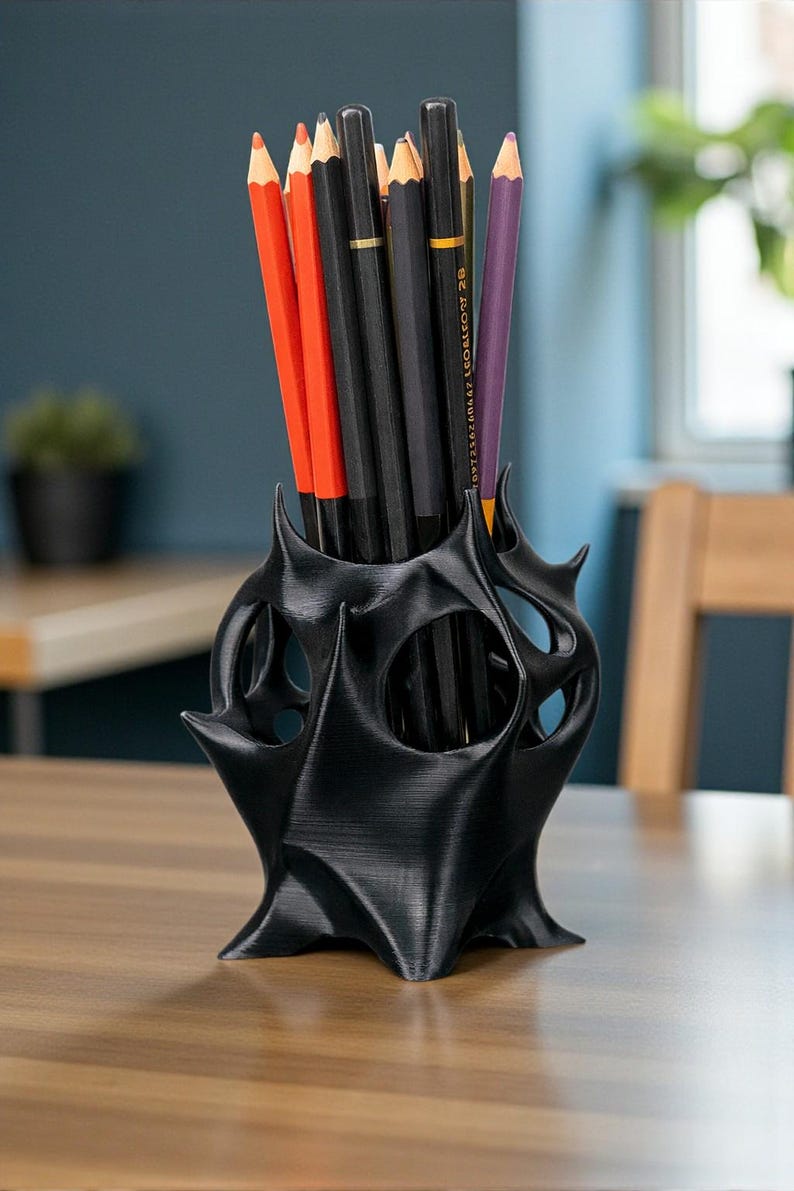 May include: A black, 3D-printed pencil holder with a unique, spiky design. The holder contains several pencils in various colors, including red, black, and purple. The pencils are of standard size, approximately 7.5 inches long.