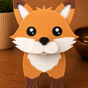 May include: A whimsical, orange fox figurine with a white chest and face, black eyes, and a black nose. The fox has brown accents on its ears and feet. The figurine is standing on a wooden surface.