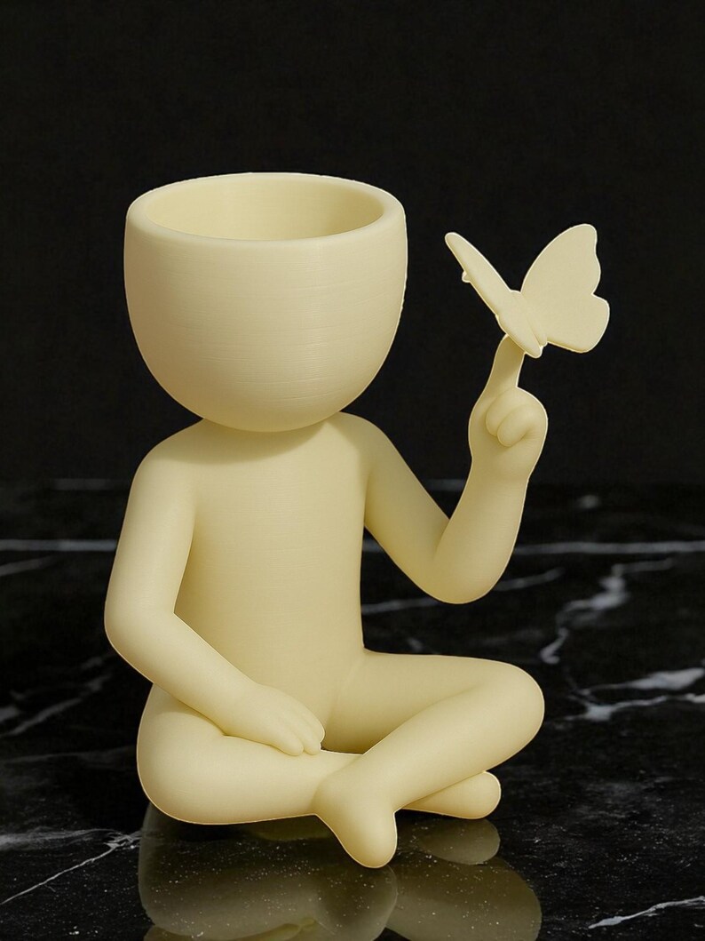 Puede incluir: Figura de color crema de una persona sentada, con la cabeza hueca y una mariposa posada en un dedo. La figura es lisa y tiene un dise&ntilde;o minimalista, adecuada para la decoraci&oacute;n del hogar o como un regalo &uacute;nico.