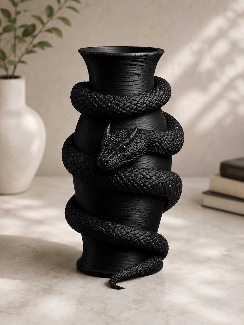 May include: A black vase with a textured surface, encircled by a detailed, sculpted black snake. The snake's head is visible, adding a striking contrast to the vase's smooth form. The vase is a decorative home accent.