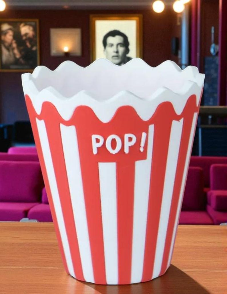 May include: A red and white striped popcorn container with a scalloped rim. The word "POP!" is printed in white on the front. The container is designed to resemble a classic popcorn bucket.