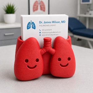 May include: A red, lung-shaped business card holder with a smiling face design. The holder contains white business cards with the text "Dr. James Wilson, MD, Pulmonologist" and contact information. A medical-themed desk accessory.