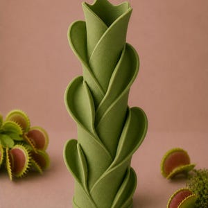 May include: A green, cylindrical vase with a layered, leaf-like design. The vase is a light green color and has a textured surface. Several Venus flytraps are scattered around the vase, with green leaves and red interiors.