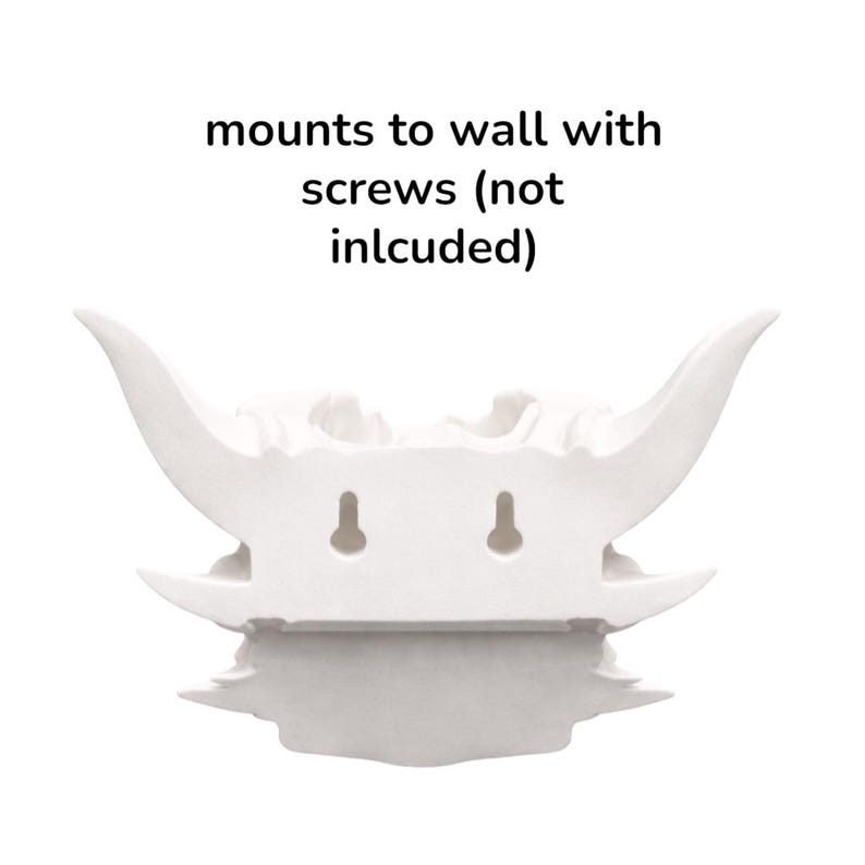 Puede incluir: Escultura decorativa blanca para montar en la pared con dise&ntilde;o de calavera con cuernos. La escultura tiene dos ranuras para colgar y el texto "mounts to wall with screws (not included)".