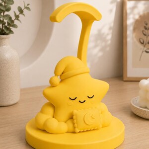 May include: A yellow star-shaped night light with a sleeping cap and a crescent moon design on a pillow. The lamp has a curved arm and sits on a round base. The lamp is made of a soft material.