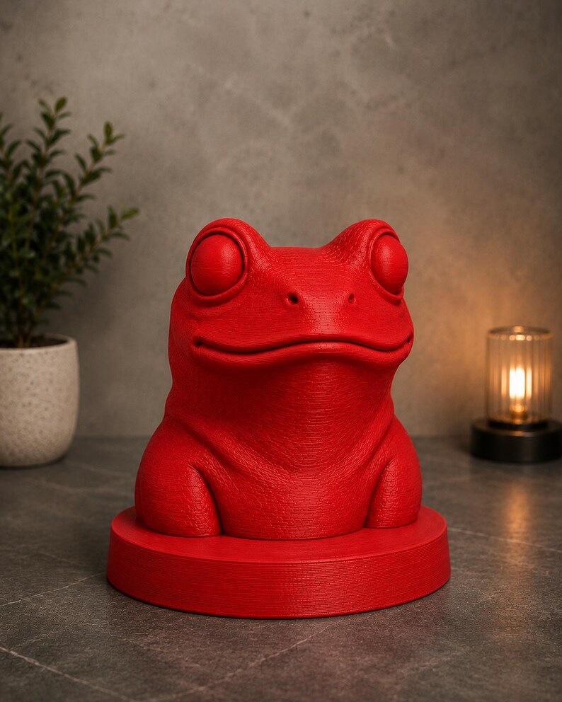 May include: A vibrant red frog sculpture with large, round eyes and a textured surface. The frog sits atop a matching red circular base. The sculpture is a decorative item, suitable for home decor.