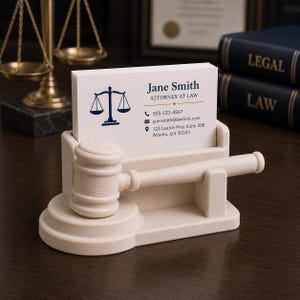 May include: A light-colored wooden business card holder shaped like a gavel and stand. The holder displays business cards with the name "Jane Smith, Attorney at Law" and contact information. A golden scale is visible in the background.