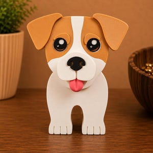May include: A 3D-printed dog figurine with a white body, brown ears, and a brown patch on its head. The dog has large black eyes, a black nose, and a pink tongue. The figurine is standing on a wooden surface.