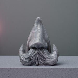 May include: A gray sculpture of a nose and mustache. The nose is a triangular shape, and the mustache has curled ends. The sculpture is on a gray surface against a gray background.