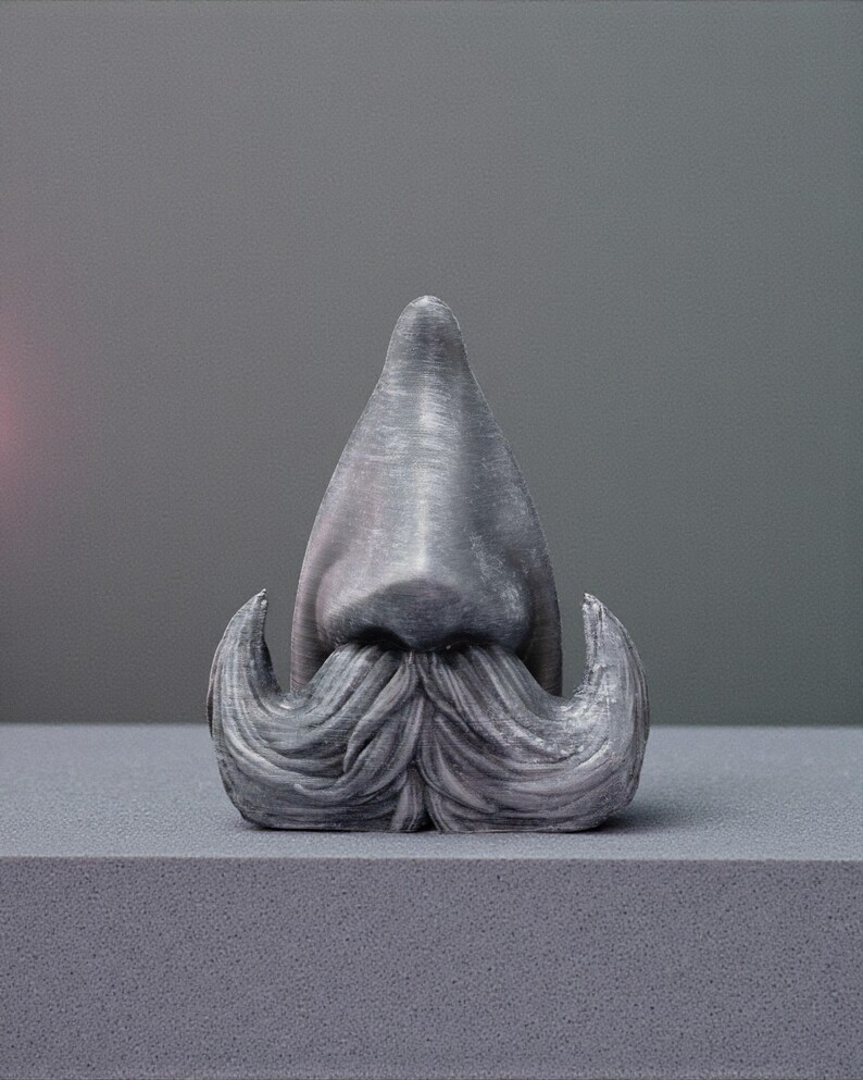 May include: A gray sculpture of a nose and mustache. The nose is a triangular shape, and the mustache has curled ends. The sculpture is on a gray surface against a gray background.